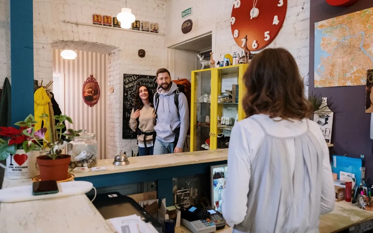 Recepcionista de pousada recebendo um casal de mochileiros no balcão